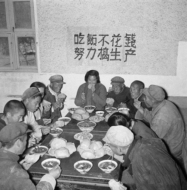 人民公社公共食堂,墙上标语:「吃饭不花钱,努力搞生产」。敞开吃的承诺只维持了几个月——高征购掏空粮仓,食堂断炊之时,就是