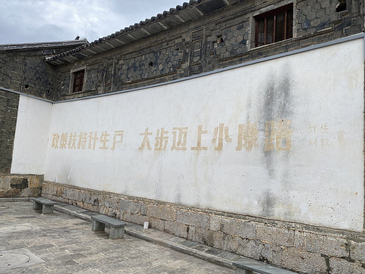 云南大理的老墙上,计生标语正在褪色:「政策扶持计生户,大步迈上小康路」。政策已经掉头催生,墙上的字却来不及改——标语会褪