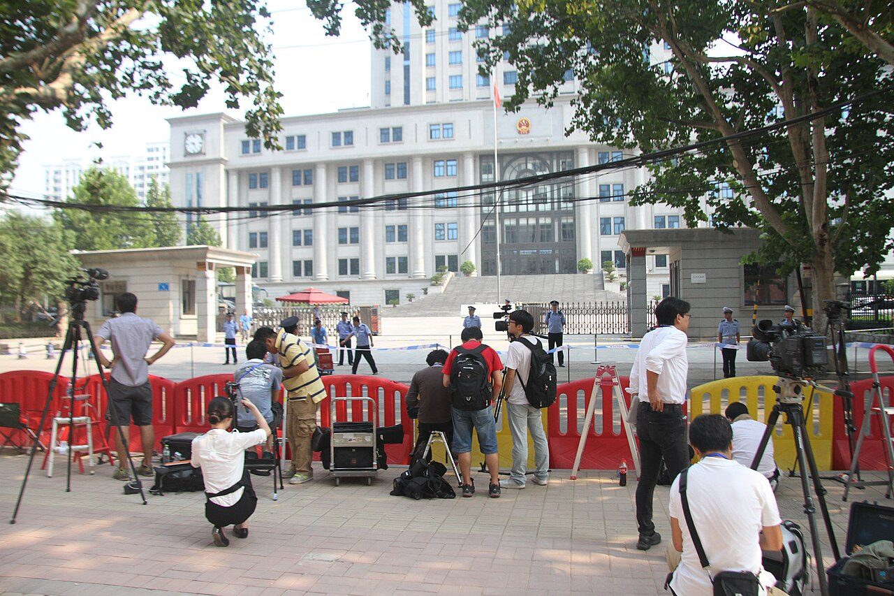 2013 年 8 月,济南中院门外:薄熙来案开庭,中外媒体被拦在警戒线外,在烈日下守候。公众能围观的只有法院的大门——庭